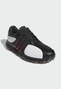 Czarno-białe obuwie sportowe o smukłym designie, skórzana cholewka, fakturowane akcenty, czerwone detale oraz podeszwę z kolcami.