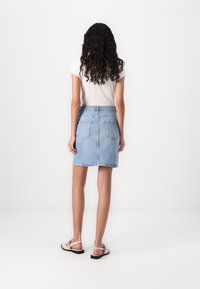Jeanskjørt i lyseblå, knelangt, med tettsittende midje og to baklommer. Kombinert med en hvit topp og lyse sandaler.