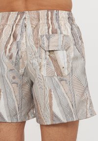 Shorts de bain pour hommes avec un design texturé et à motifs dans des teintes de beige, gris et blanc, équipés d'une poche latérale et d'une taille élastique.