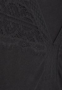 Tissu noir avec un délicat détail en dentelle florale superposée et une finition en maille, montrant une section d'un vêtement près d'un décolleté en V.