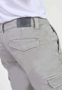 Lichtgrijze cargoshorts hebben een gestructureerde afwerking, riemlussen, een achterzak met klep en een merklabel op de tailleband.