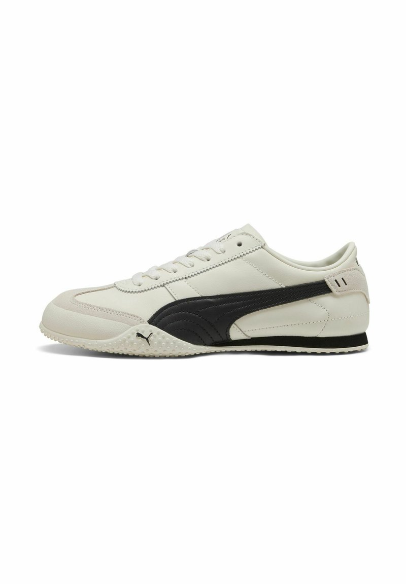Zapatillas deportivas en blanco y negro con un empeine de cuero liso, puntera redondeada, suela de goma texturizada y un diseño de franjas laterales en contraste.