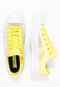 Baskets en mesh jaune avec semelles en caoutchouc blanches, dotées de lacets jaunes et d'un dessus transparent à motifs. Marquage de la semelle intérieure noir visible.