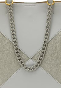 Lys grå tote bag med kædehåndtag, tekstureret materiale og et geometrisk design med glatte og småstensoverflader. Gyldne metaldetaljer.
