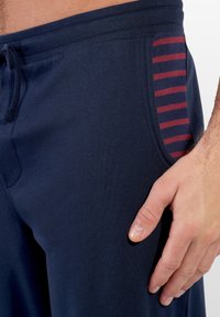 Marineblå joggers lavet af blødt stof med elastisk talje og snøre, der har en side lomme med en stribet rød accent.