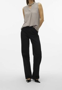 Top senza maniche di un grigio chiaro, con scollo a V e tessuto testurizzato, abbinato a pantaloni neri a vita alta. Tacchi a punta neri completano il look.