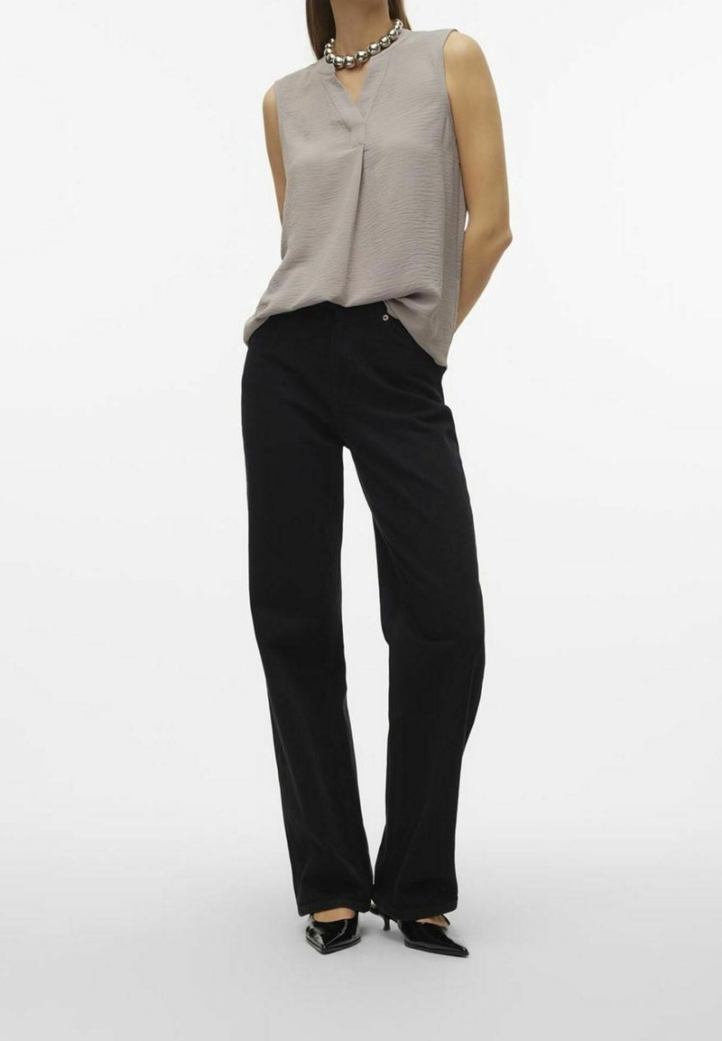 Top senza maniche di un grigio chiaro, con scollo a V e tessuto testurizzato, abbinato a pantaloni neri a vita alta. Tacchi a punta neri completano il look.
