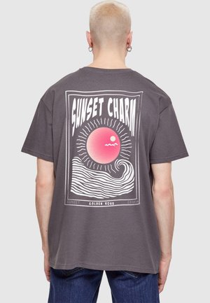 Grå bomulds t-shirt med et stort grafisk print af en pink sol over bølger, med teksten "SUNSET CHARM" i fede hvide bogstaver.
