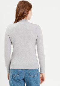 Pull en maille gris avec des manches longues, col et ourlet côtelés. Texture douce avec un design ajusté et un minimum de détails.