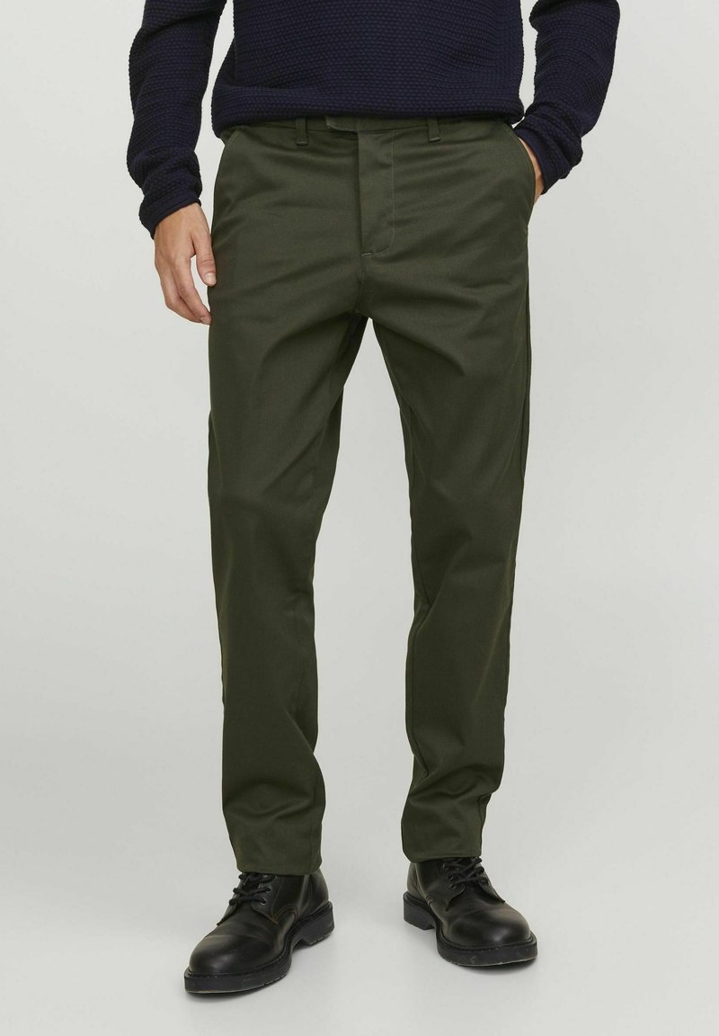 Pantaloni ușori, de un verde închis, cu un design drept, buzunare frontale și bucle pentru curea, asortați cu bocanci negri cu șireturi.