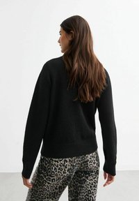 Zwarte gebreide trui met lange mouwen, geribbelde manchet en zoom. Gepaarde met een broek met panterprint in grijs en zwart. Neutrale achtergrond.