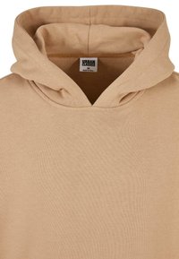 Felpa con cappuccio in cotone beige dal tocco morbido, con una scollatura ampia e un'etichetta cucita all'interno. Senza motivi o accenti prominenti.