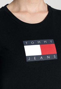Svart bomullströja med en rektangulär logotyp med texten "TOMMY JEANS" och färgblock i rött, vitt och blått i mitten.