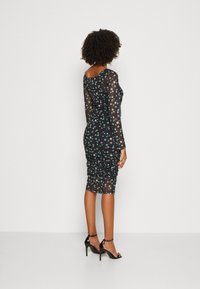 Zwarte mesh jurk met groene en witte bloemenpatronen, lange mouwen, getailleerde silhouet en geplooide details aan de achterkant.