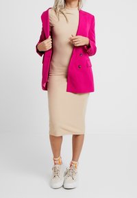 Růžový dvouřadý blazer přes béžové ribbed midi šaty, doplněný béžovými teniskami a multibarevnými pruhovanými ponožkami.
