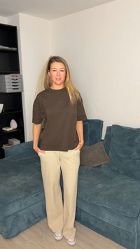 Brun t-skjorte med korte ermer kombinert med beige bukser med vide ben. Kjennetegnes av en avslappet passform og subtil tekstur. Bakgrunnen har en grønn sofa.