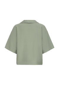 Blouse à manches courtes, verte clair, en tissu texturé. Elle présente un col classique et une coupe décontractée, avec un ourlet droit à l'arrière.