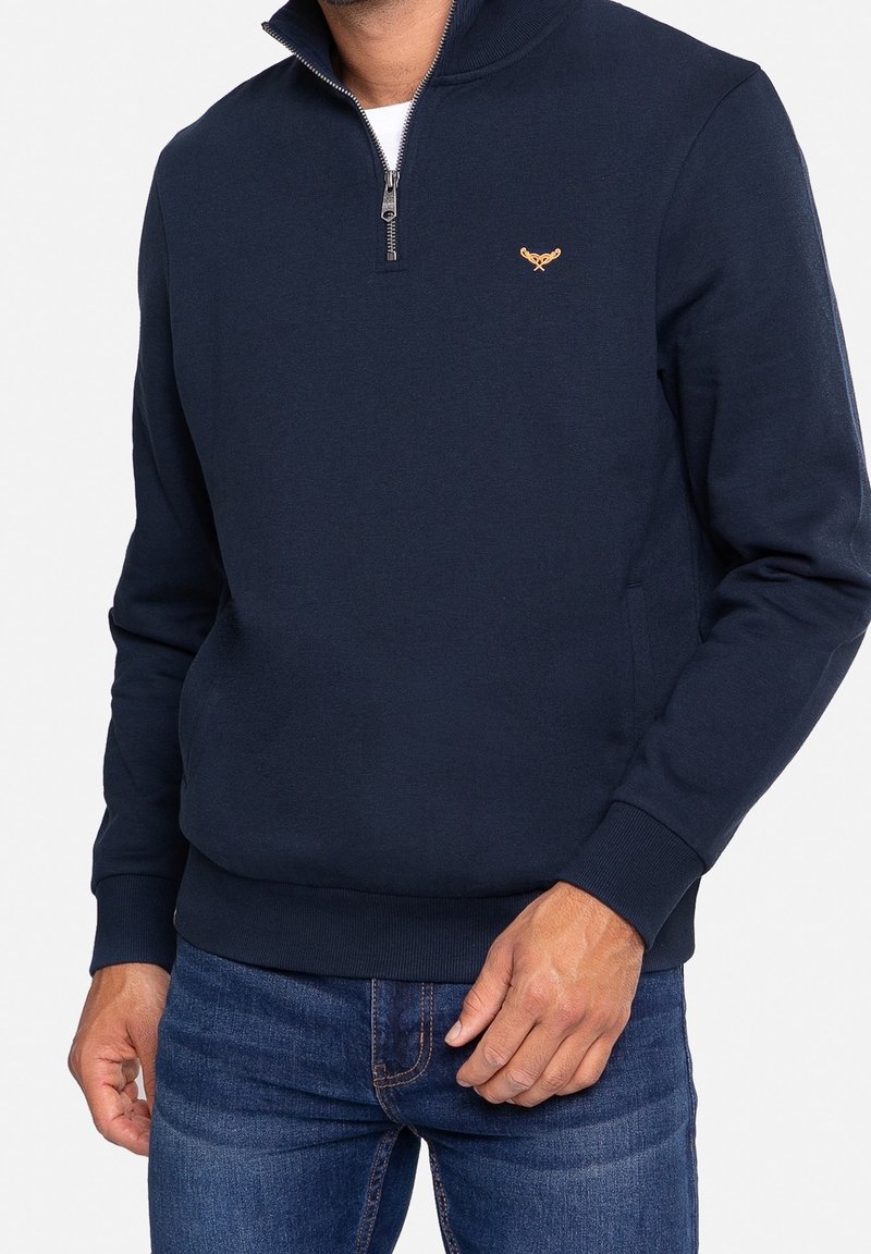 Felpa zip-up blu navy realizzata in tessuto morbido, con colletto alto, polsini a costine e un piccolo logo ricamato sul petto.