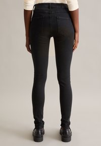 Czarne rurki z wysokim stanem o fakturowanej powierzchni, z dwiema tylnymi kieszeniami i gładką, dopasowaną sylwetką do kostek.