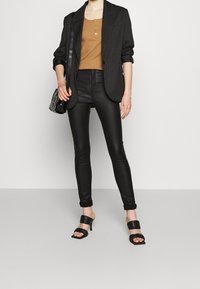 Sorte pinstriped blazer over en brun ribbet henley-top, parret med tætsiddende sorte læderbukser og sorte hælede mules, mens der holdes en sort taske.