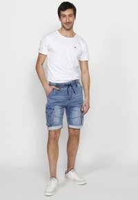 Lysblå denim shorts med oprevne kanter, med flere lommer, en drawstring i taljen, parret med en simpel hvid t-shirt og hvide sneakers.