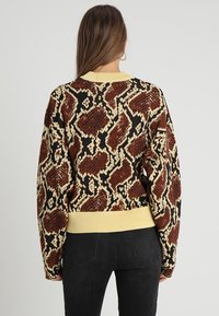 Strickpullover mit einem strukturierten, braun-weißen Tiermotivdesign und einem gelben Rippenbund sowie Kragen; lockere Passform.