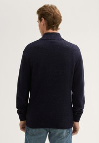 Marine blauwe gebreide trui met een hoge ribbelkraag en lange mouwen, met een textuur die versierd is met veelkleurige stippen, en een relaxte pasvorm.