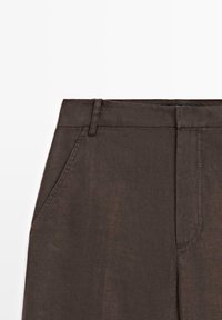 Donkere bruine broek, voorkant in beeld, met taillebandlussen, zijzak en doorgestikte gulp, op een effen witte achtergrond.