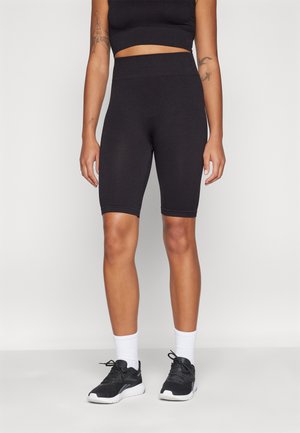 Set athletic de culoare neagră, cu un top scurt cu dungi și șorturi de bicicletă cu talie înaltă, asortat cu pantofi sport negri și șosete albe.