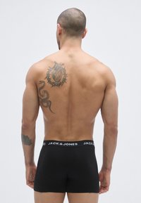 Melni kokvilnas bokseršorti ar platu, kontrastējošu jostu ar "JACK & JONES" logotipu. Modelim ir tetovējums augšējā muguras daļā.