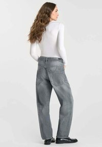 Jeans larges gris en denim, dotés de deux poches arrière, d'une taille haute et d'une coupe décontractée. Assortis à un haut blanc à manches longues.