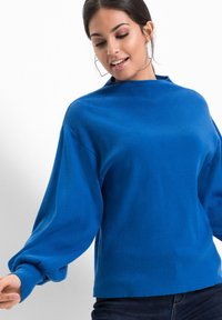 Maglione blu a maglia con collo alto, maniche a palloncino e vestibilità comoda. La trama del tessuto appare morbida ed è uniformemente colorata.