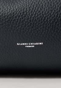 Fekete bőr, texturált felszínt kapott, amelyen fehér színű, dombornyomott „GIANNI CHIARINI FIRENZE” márkajelzés található. A hangsúly az anyagon és a részleteken van.