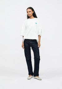 Λευκό βαμβακερό T-shirt με χαλαρή εφαρμογή και φαρδιά μανίκια, φέρει μια μικρή τουρκουάζ γραφικό. Συνδυασμένο με σκούρα τζιν και ανοιχτόχρωμα παπούτσια.