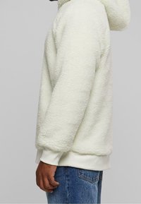 Felpa con cappuccio bianca e pelosa con tessuto morbido e strutturato, vita aderente e polsini a coste. Il design comprende un cappuccio e una vestibilità comoda.