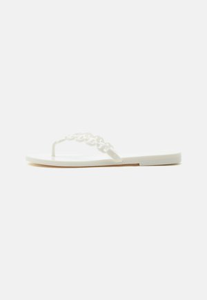 White flat sandal with a thin sole and a decorative linked chain strap crossing the foot and a toe post.