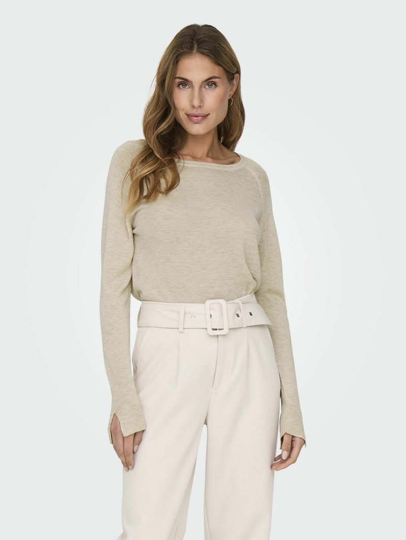 Helle beige, langärmlige Strickoberteil mit entspanntem Ausschnitt, kombiniert mit hoch taillierten weißen Hosen mit breitem Gürtel und Seitenschlitzen.