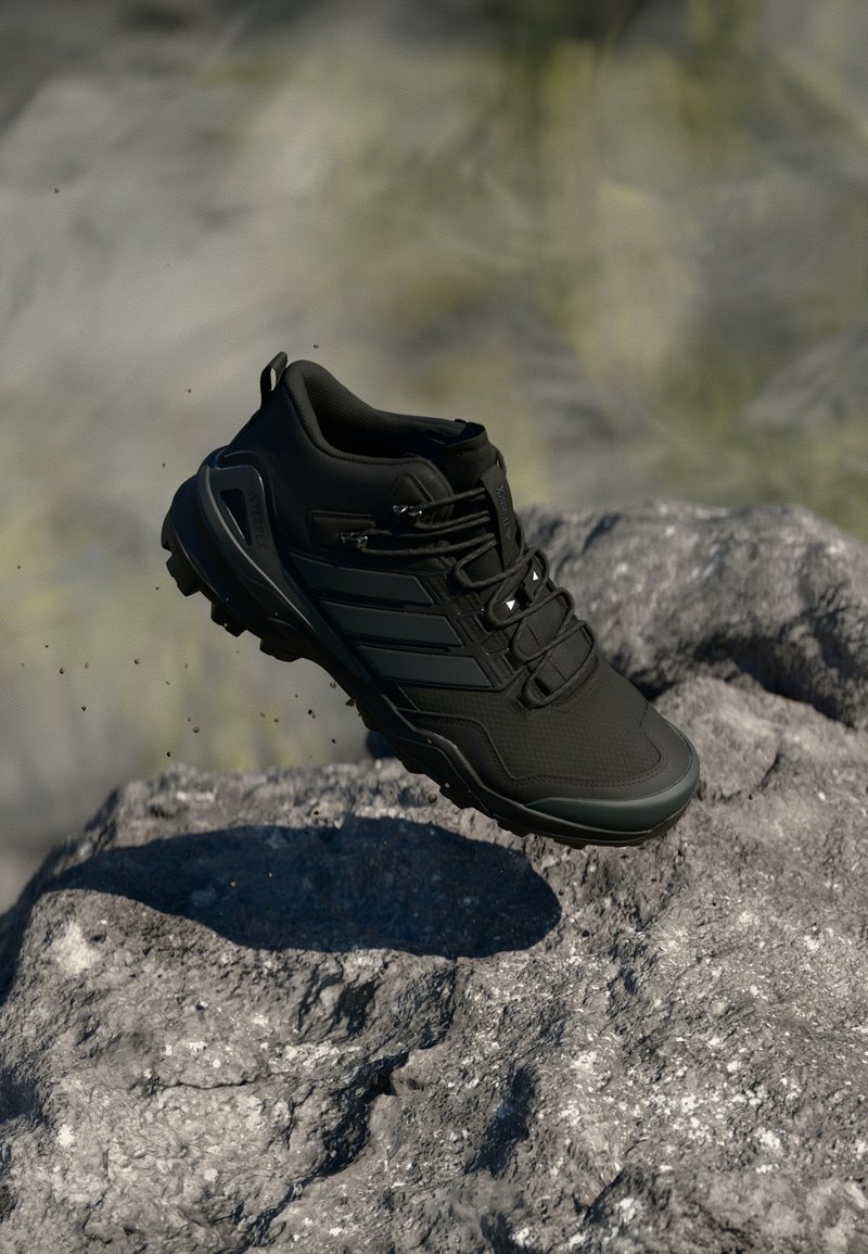 Schwarzer Trail-Laufschuh mit robustem Profil schwebt über einer felsigen Oberfläche, Staubpartikel sind in der Außenszene sichtbar.