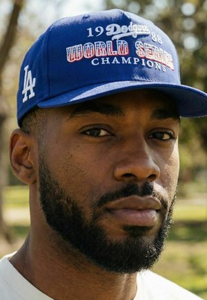 Homme barbu portant une casquette de baseball bleue « 1988 Dodgers World Series Champions », en extérieur avec des arbres flous en arrière-plan.