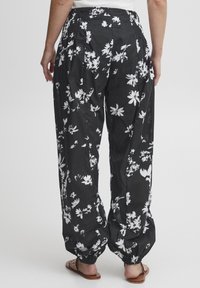 Svarta blommiga byxor med avslappnad passform, vita blommönster, elastisk midja och avsmalnande fållar. Tillverkade av lättviktsmaterial.