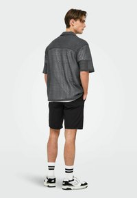 Grå t-shirt med korte ærmer og et tekstureret zigzag-mønster, parret med sorte shorts og hvide sokker med sorte striber, fuldendt med sporty sneakers.
