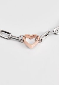 Silberne Gliederketten mit einer zentralen Roségold-Herzverbindung, die auf einer Seite mit einer gravierten Inschrift versehen ist, glatte Oberfläche und glänzende Ausführung.