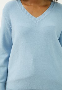 Hellblauer Pullover mit V-Ausschnitt, langen Ärmeln und strukturiertem Strickmuster. Weiches Material mit subtilen Schimmerdetails.