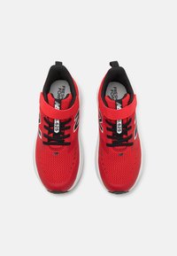 Baskets de sport rouges avec une tige en maille, des accents noirs, une sangle Velcro et une semelle blanche rembourrée. Logo de la marque visible sur les côtés.