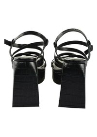 Black heeled sandals feature a crocodile texture, cross straps, and a chunky square heel. The design is sleek and minimalistic.