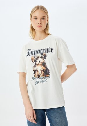 T-shirt en coton blanc avec une illustration de chiot imprimée, accompagnée du texte "Innocence" et "De tels regards réchauffent votre cœur" en dessous. Coupe décontractée.