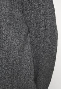Pull en tricot gris affichant une surface texturée, avec une coupe légèrement ample et un subtil motif côtelé le long des bords. Aucun matériel ou accent visible.