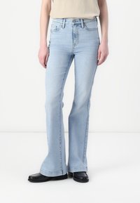 Lyseblå utsvingte jeans i denim med høy midje og klassisk fem-lommers design. Kombiner med svarte flate sko med frynsekant.