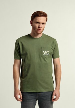 Camiseta de algodón verde con mangas cortas, que presenta un bolsillo en el lado izquierdo del pecho con la inscripción "VC" en texto blanco y amarillo. Corte clásico.