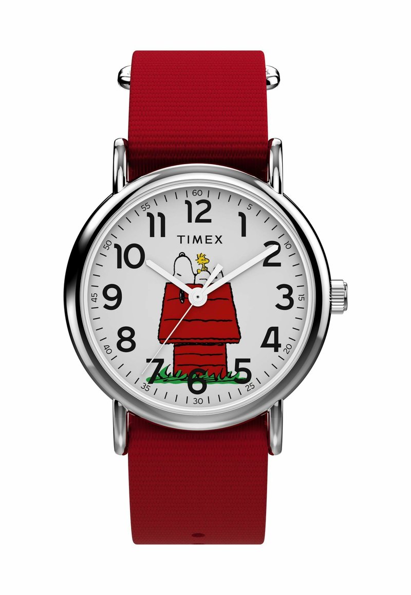 Reloj Timex con una esfera blanca que presenta una ilustración de Snoopy y una casita de perro roja. Correa de tela roja, caja de metal en tono plateado, números árabes en negro.